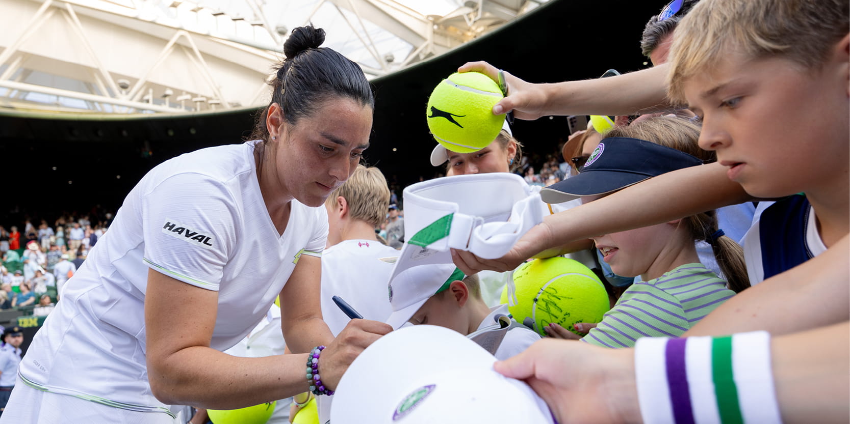 Women's tennis player Ons Jabeur singing fan autographs on Centre Court at Wimbledon in 2023 after a tennis match