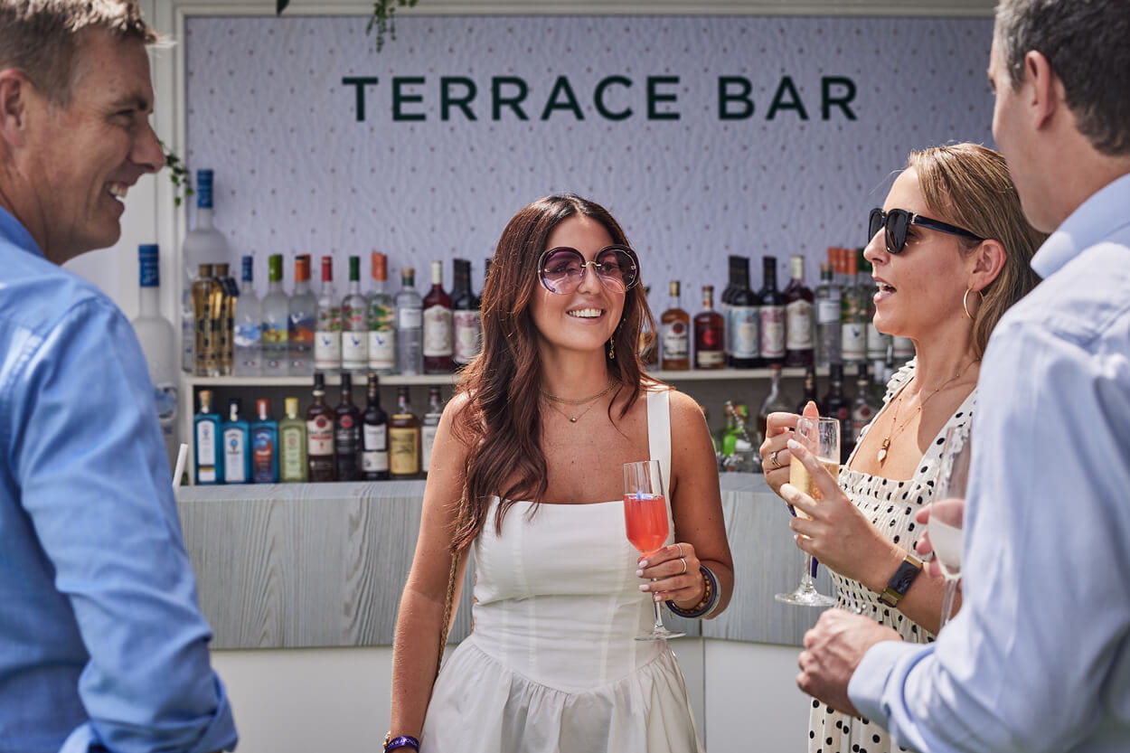 Guests drinking cocktails in The Lawn garden at Wimbledon in dresses and sunglasses