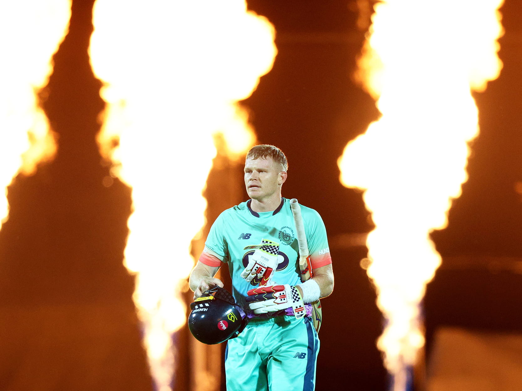 Oval Invincibles men's cricket player walking out for a match in The Hundred tournament with fire behind him