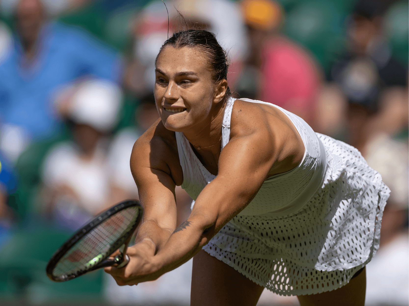 Women's tennis player Aryna Sabalenka stretching to hit a tennis ball at Wimbledon