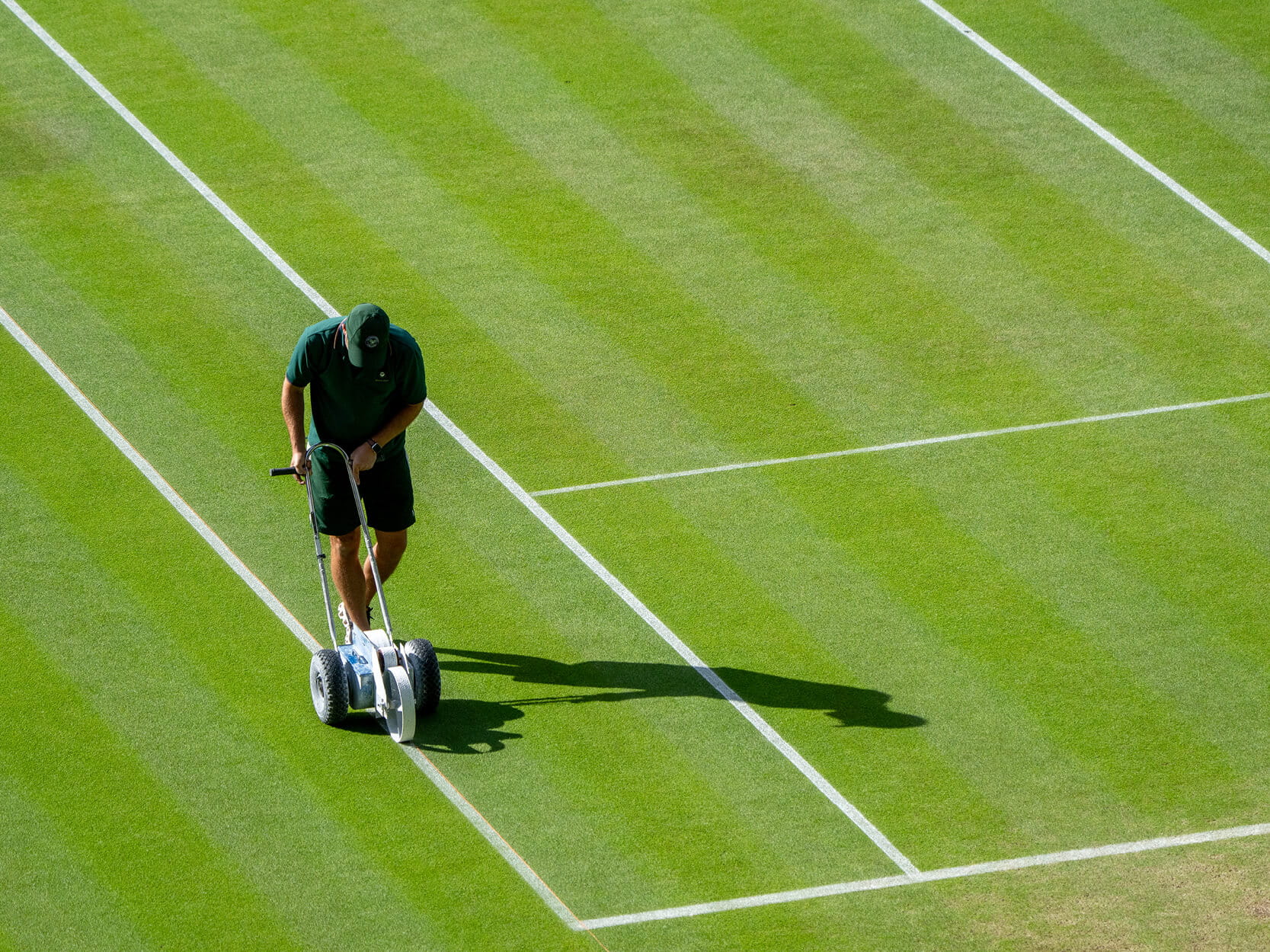 A Wimbledon groundsman marking the white lines on the Centre Court at The Championships Wimbledon before the players match