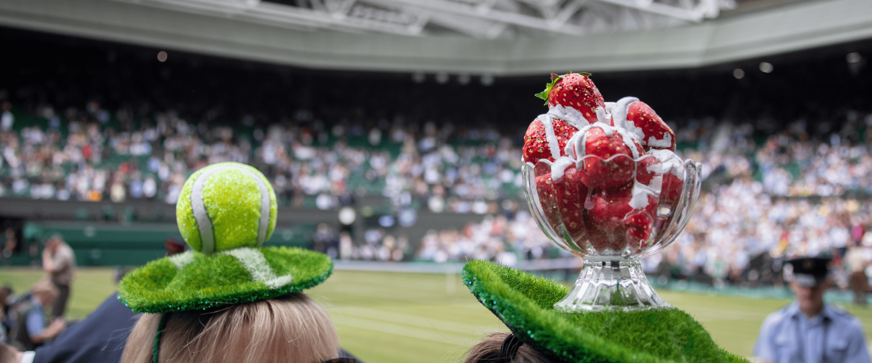 Tennis fans at Wimbledon on Centre Court wearing tennis ball and strawberries and cream hats while watching the tennis