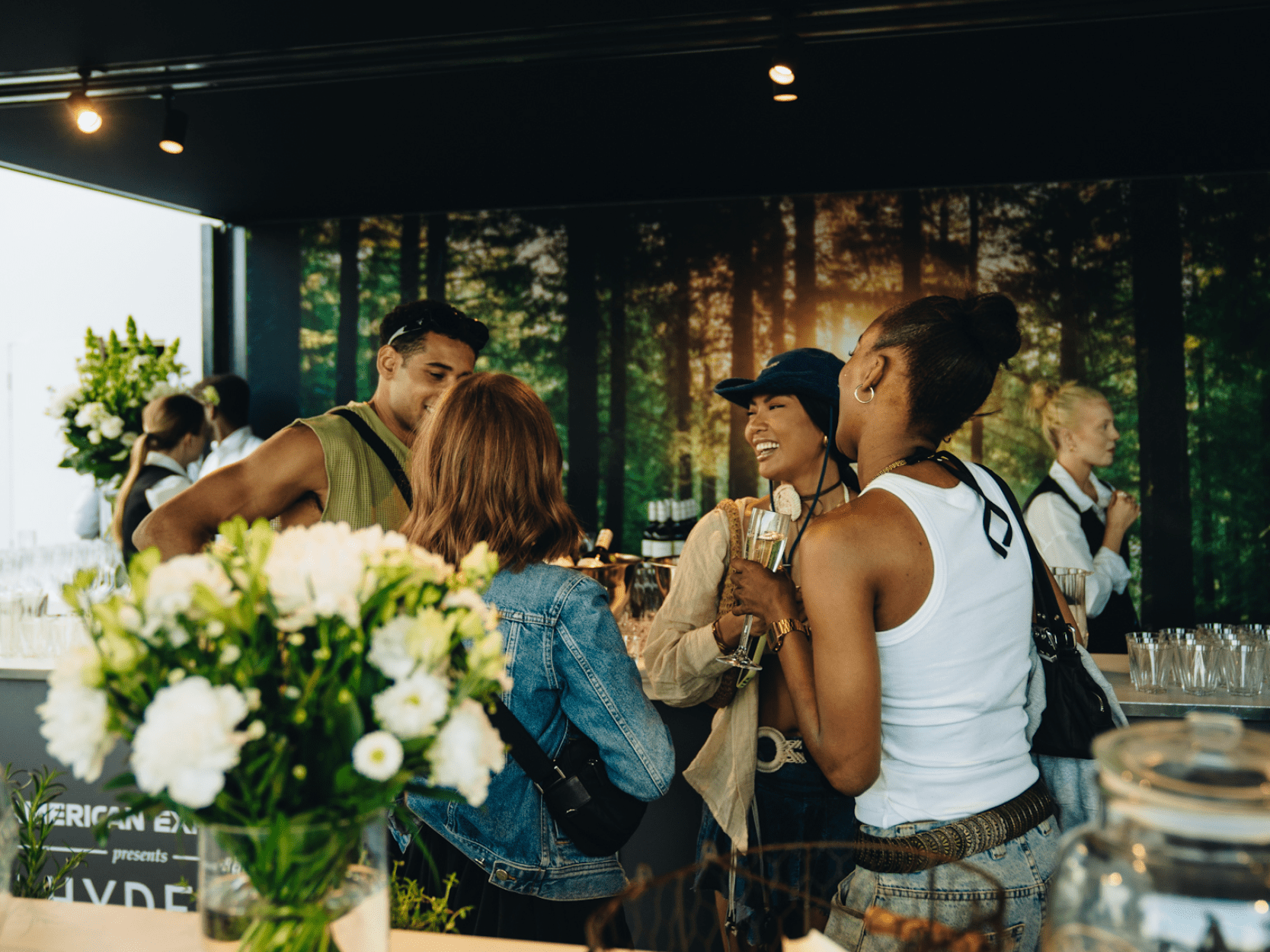 Group of friends chatting and laughing by the bar in the Great Oak Roof Garden hospitality at BST Hyde Park