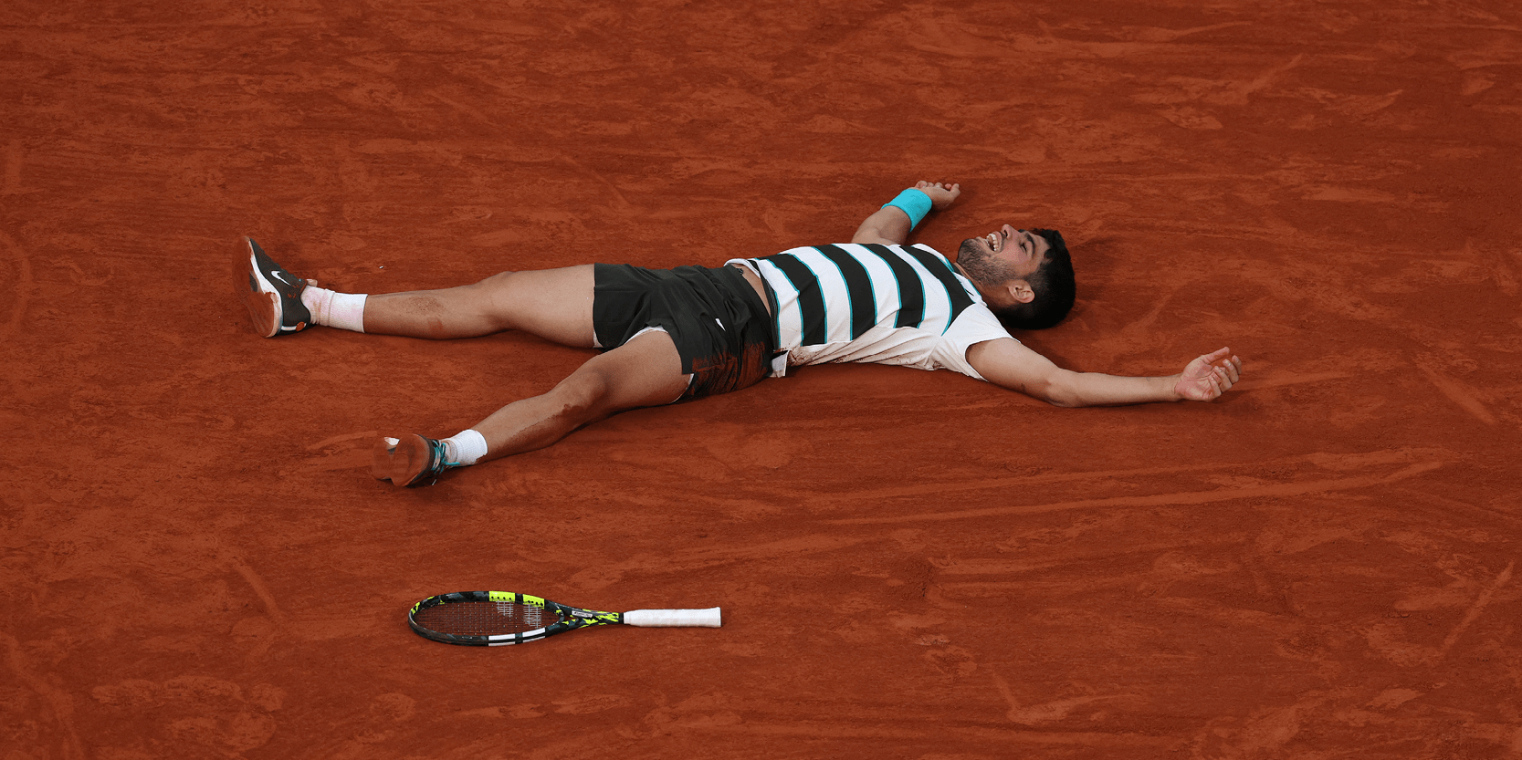 Spanish men's tennis player Carlos Alcaraz collapsing to the floor on court after winning the championship point in the final at the Roland Garros French Open 2025 celebrating