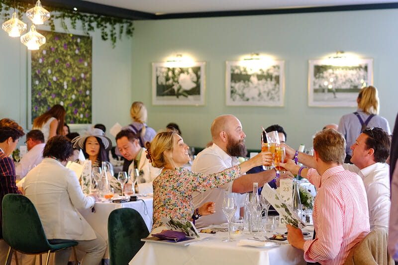 Guests sitting down for a meal doing cheers in Rosewater Pavilion at Wimbledon