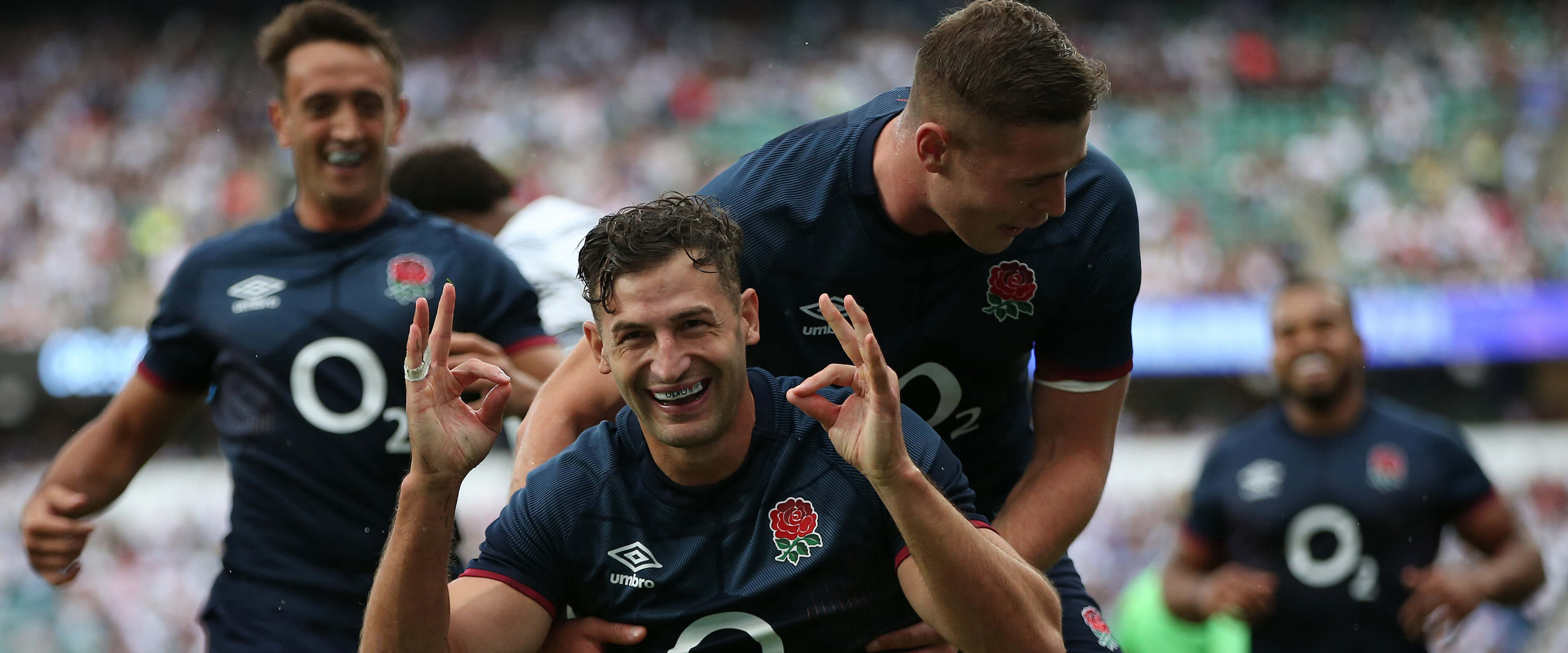 Players Jonny May, Freddie Steward and Alex Mitchell celebrating scoring in a rugby match against Japan at Twickenham Stadium