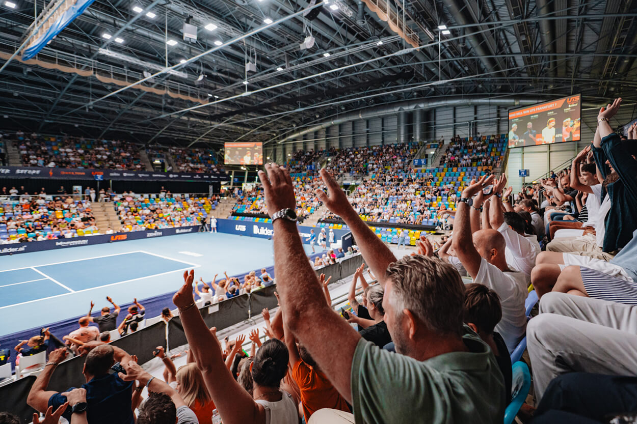 View of the tennis court at UTS tennis tournament from the crowd seats with fans hands in the air