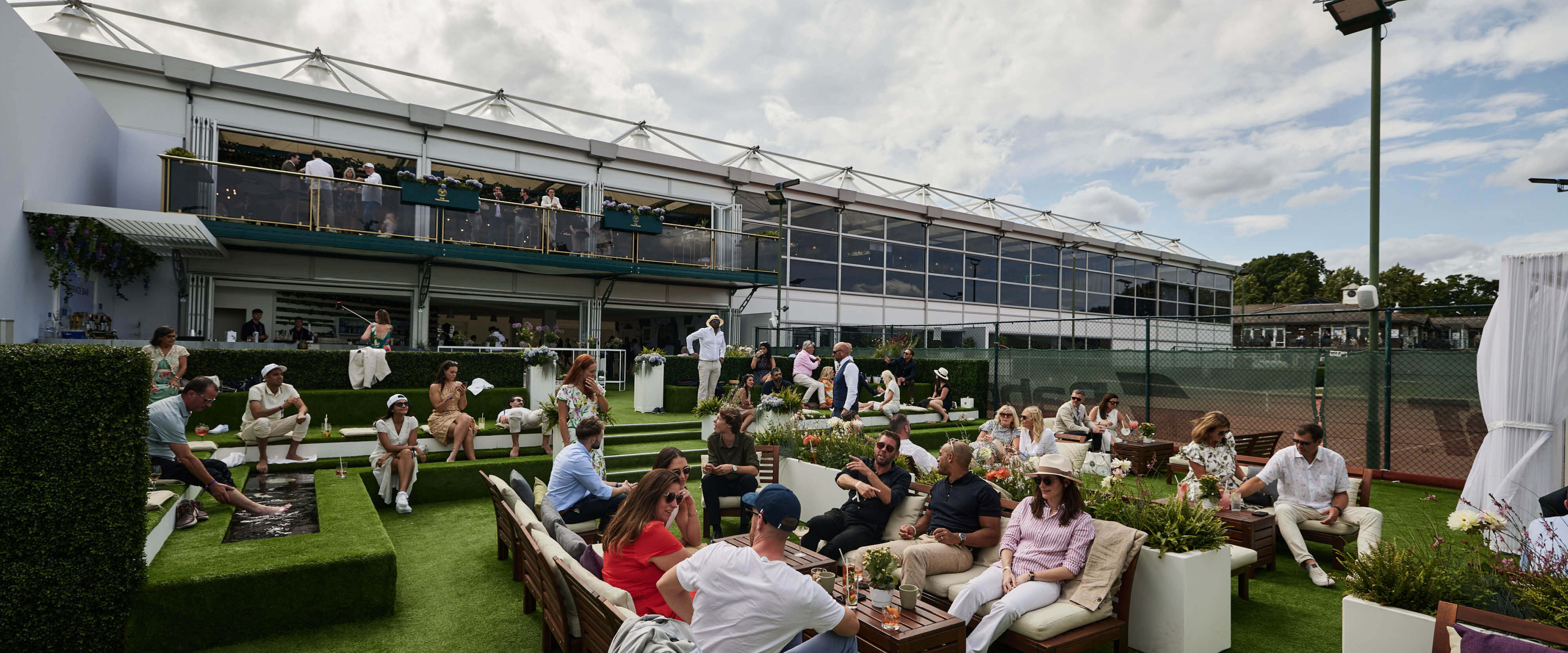 Guests seated in The Lawn English Garden on sofas enjoying drinks and listening to music at The Championships Wimbledon