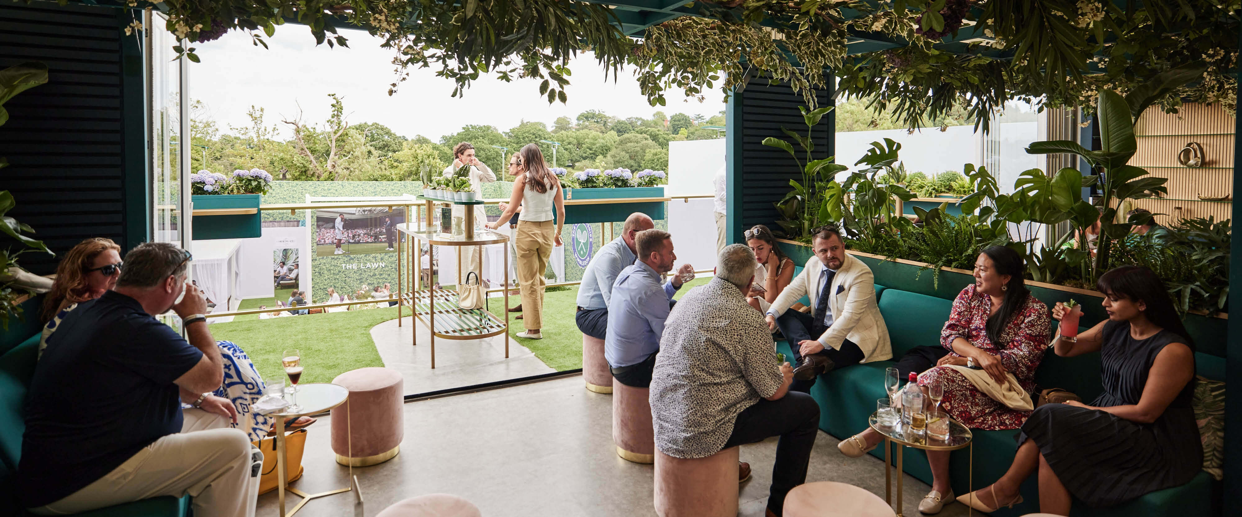 Guests sat in the Treehouse hospitality facility enjoying food and drinks by the balcony at The Championships Wimbledon